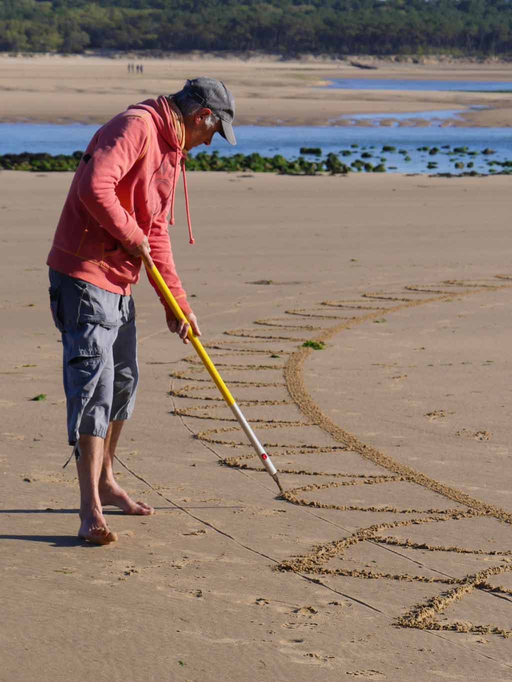 Avec son râteau, le jeune beach artiste dessine le sable sur les plages de  Saint-Brevin